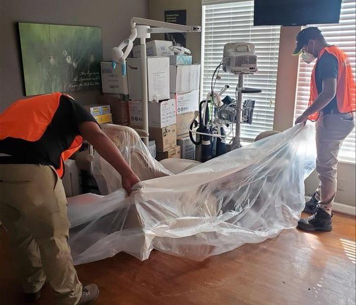 Two employees in orange vests placing protective plastic on dental equipment