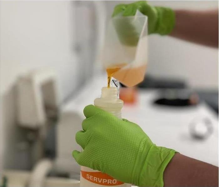Shows the hands of a scientist pouring chemical into a jug.