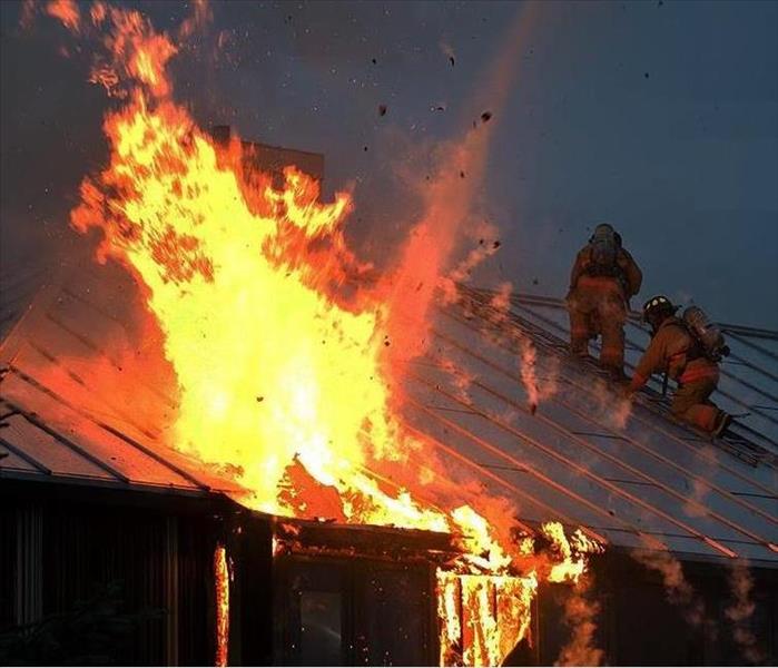 A home on fire with two firefighters fight the blaze from the roof and one firefighter on a ladder