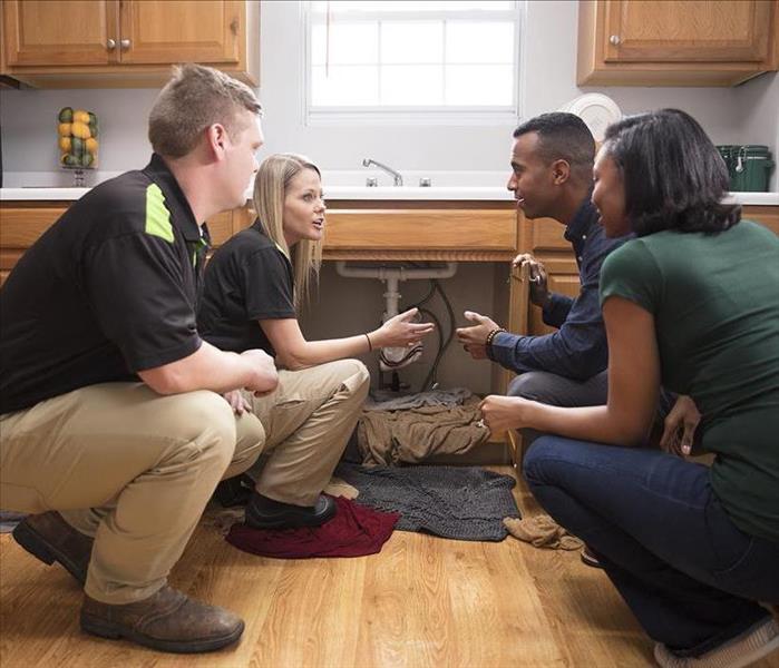 2 Servpro employess along with 2 homeowners. In Kitchen crouching near kitchen sink.