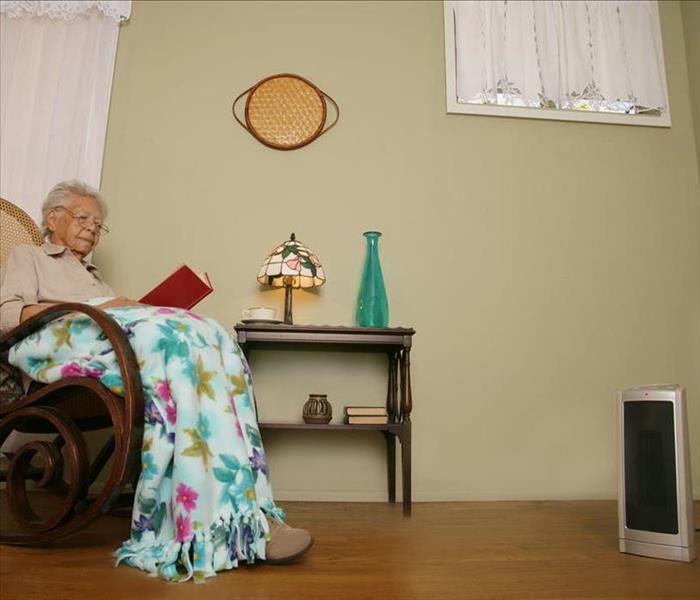Old lady in rocker chair reading a book. Space heater located 3 ft apart